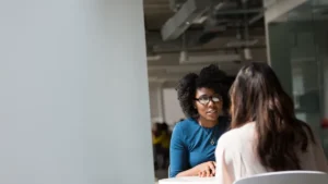 Two colleagues having a one-on-one conversation at a table in a modern office