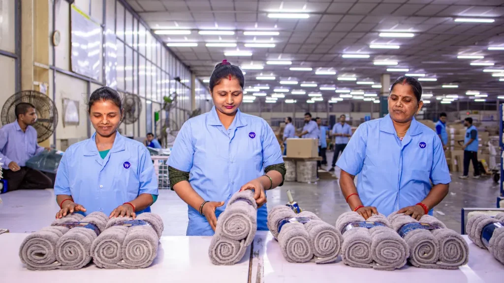 Three factory workers checking rolled towels for quality on an inspection table