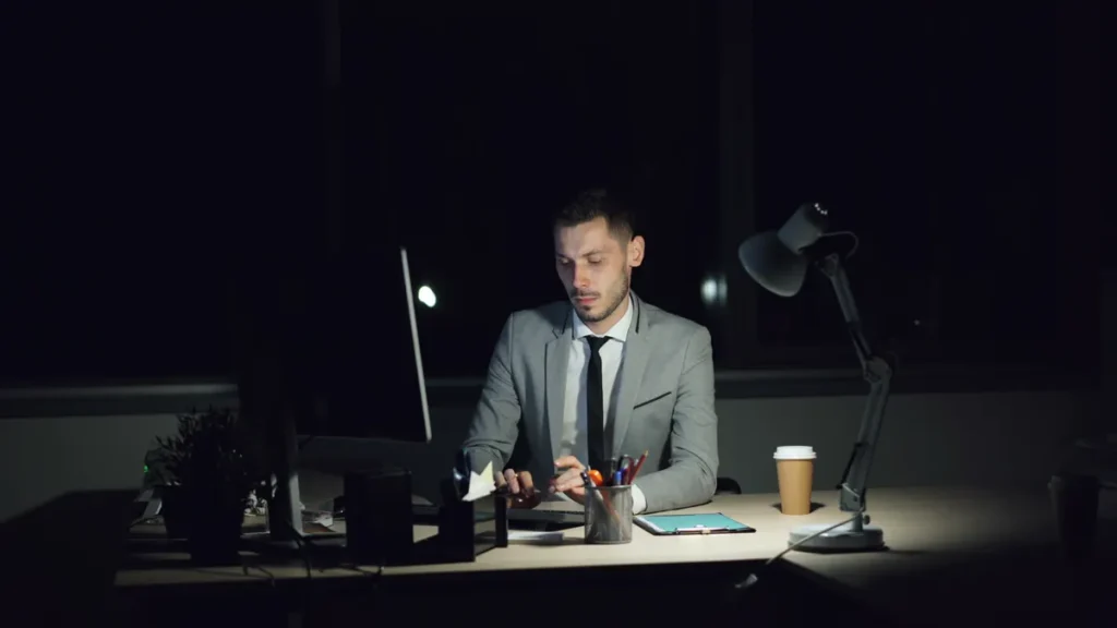 Salaried professional working late at a lamp-lit office desk after hours