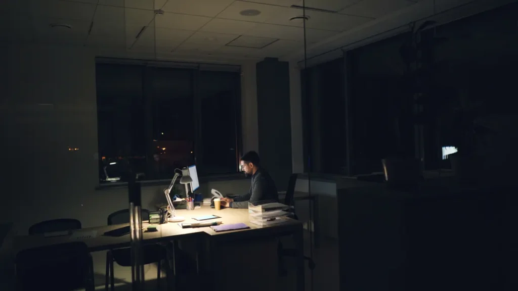 Employee working late at a lit desk in an otherwise dark office, putting in overtime hours