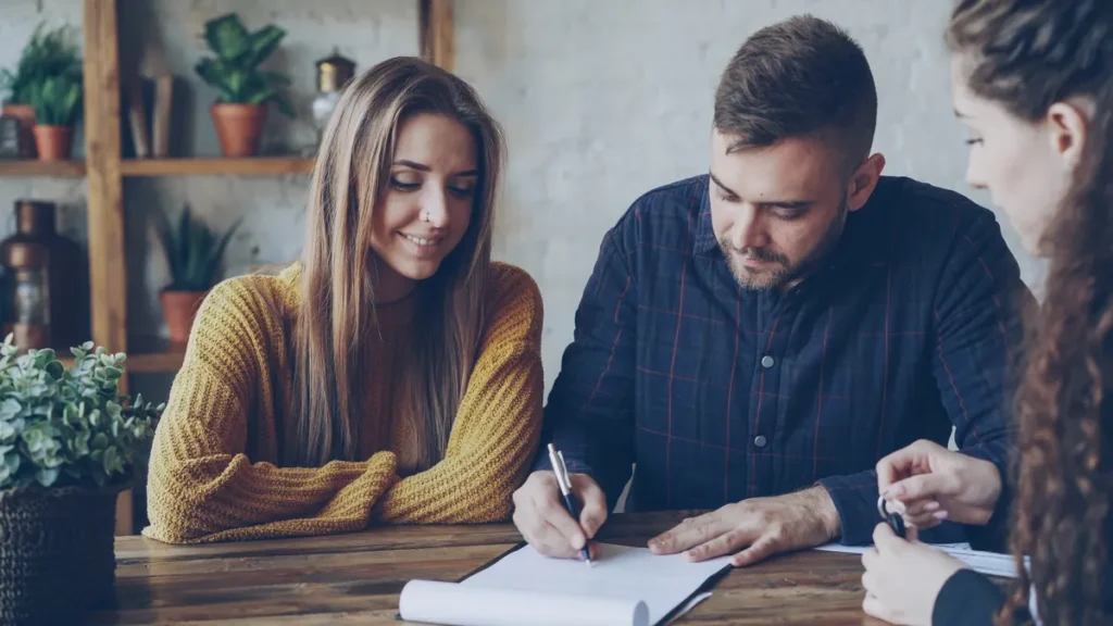 Three colleagues reviewing and signing a project agreement at a wooden table