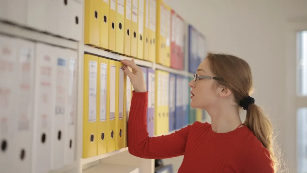 Office worker reaching for a binder on a shelf of color-coded procedure folders