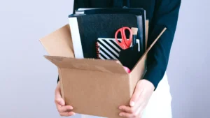 Employee carrying a cardboard box of office supplies and folders on their last day