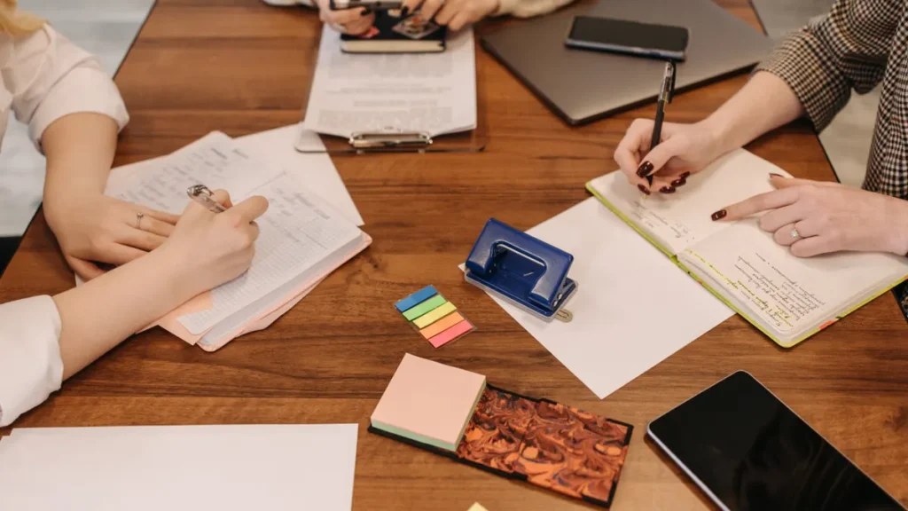 Colleagues around a wooden table taking notes on paper during a team meeting