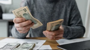 Business owner counting dollar bills at a desk with a calculator and paperwork