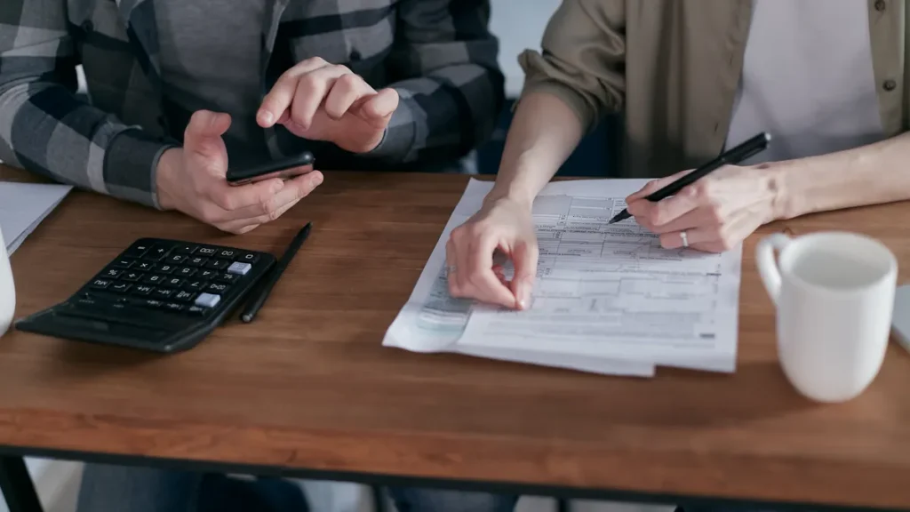 Two people reviewing tax paperwork with a calculator and pen at a wooden table
