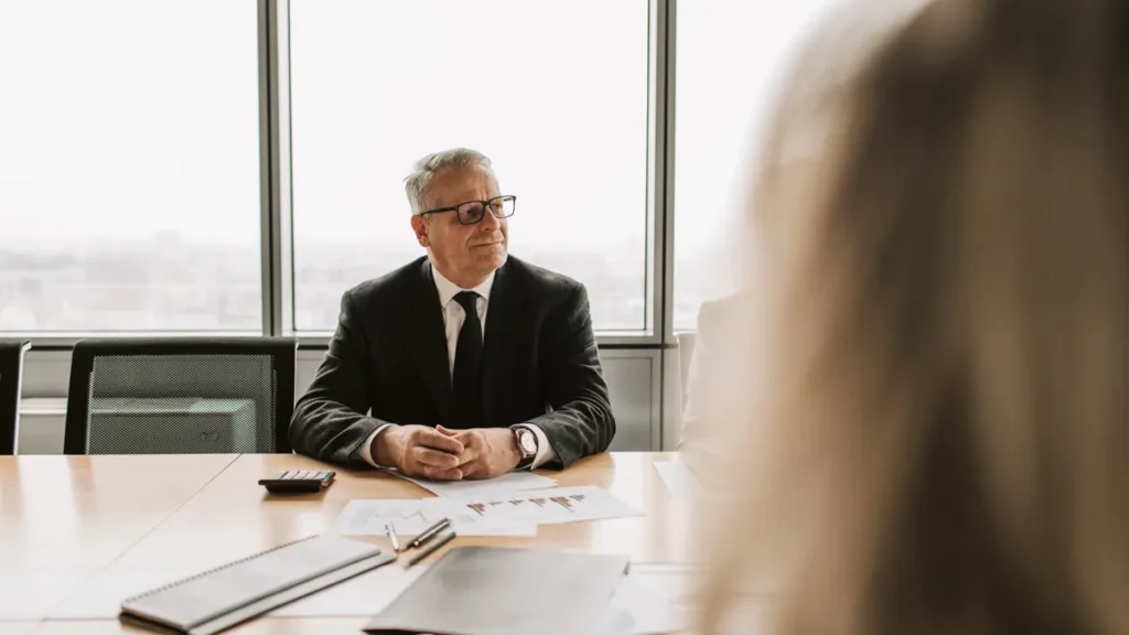 Senior executive in a dark suit seated at the head of a boardroom table