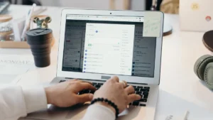 Person typing an email on a laptop at a bright desk with a coffee cup nearby