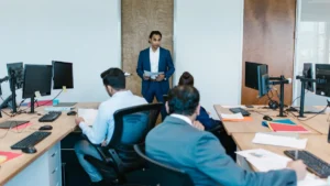 Manager standing at the front of an office addressing staff seated at their desks