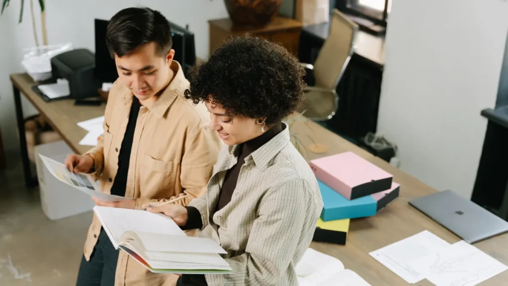 Two small business partners reviewing plans in a binder in their office